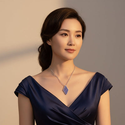 Woman wearing a dark blue dress with a necklace against a neutral background Tanzanite and diamond necklace styled on model – statement festive jewelry by Tresor Collection