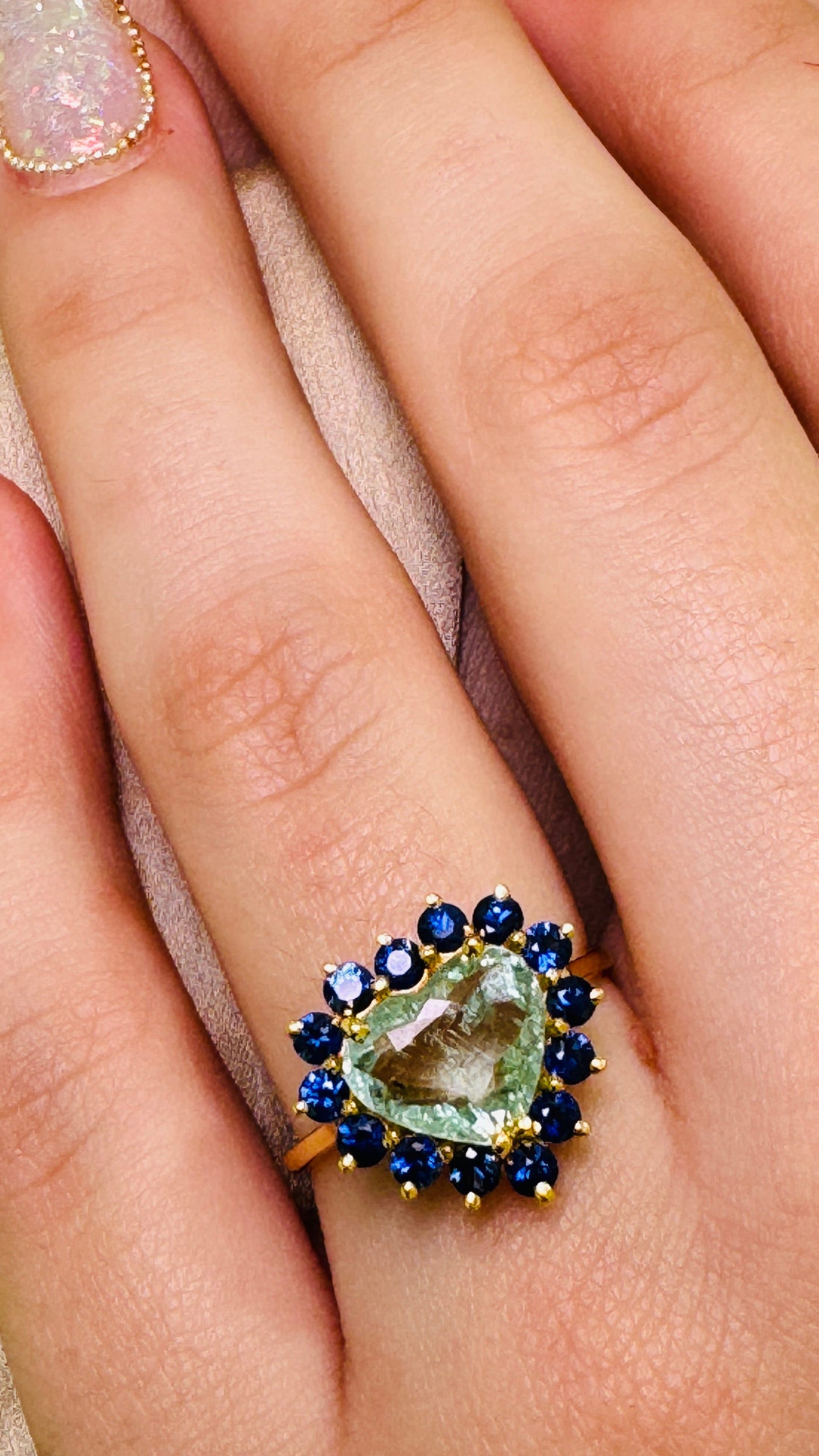 Paraiba Tourmaline Heart shape And Blue Sapphire Round Ring In 18K Yellow Gold - Tresor Collection Close-up of Paraiba tourmaline heart ring with sapphire halo worn on hand – glowing neon-blue gemstone