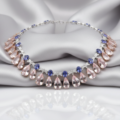 Necklace with pink teardrop-shaped stones and blue accents on a gray fabric background Close-up of 18K rose gold Morganite and Tanzanite necklace – handcrafted fine jewelry from Tresor Collection boutique