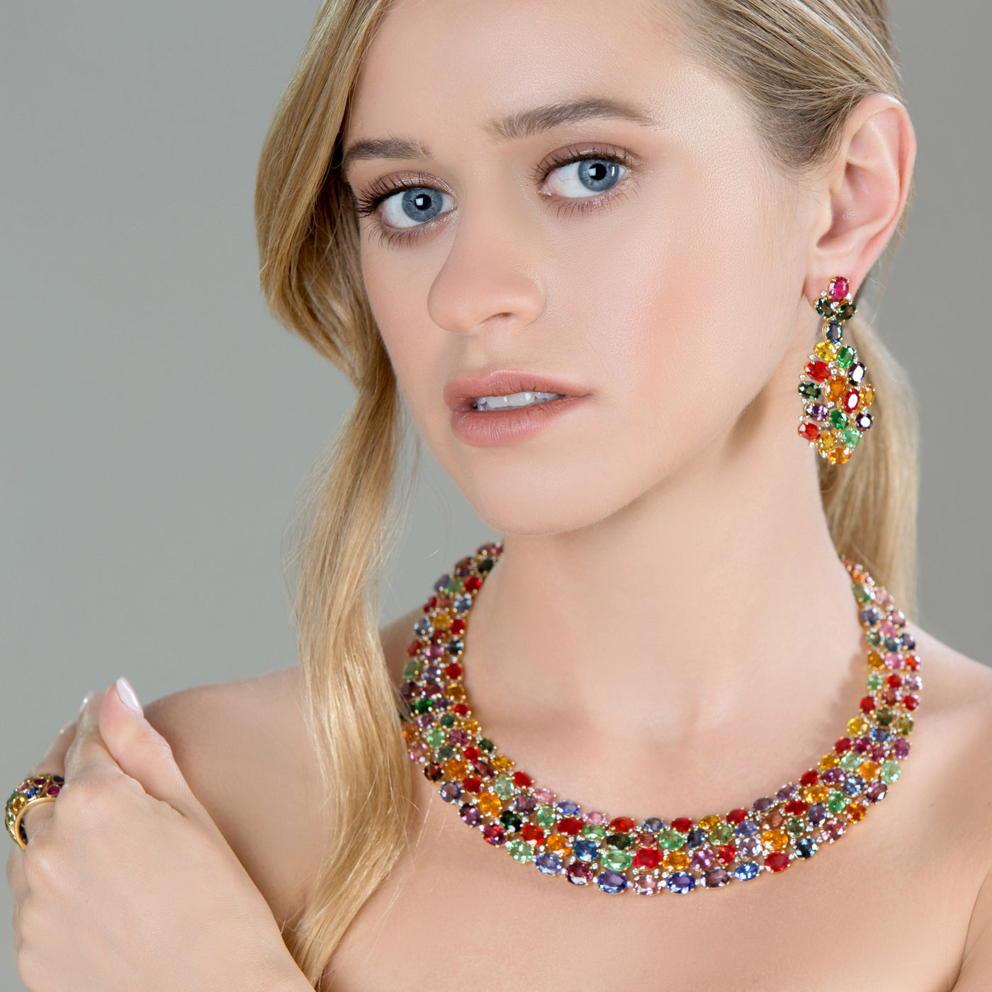 Woman wearing a colorful necklace and earrings against a gray background Elegant multicolor tourmaline necklace on model – designer gemstone jewelry for women by Tresor Collection