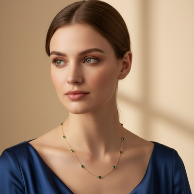 Emerald gold station necklace styled for cocktail and gifting occasions – Tresor Collection
Woman wearing a blue dress and green necklace against a beige background