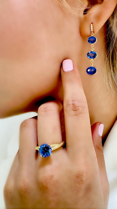 Tanzanite Oval & Diamond Earring In 18K Yellow Gold - Tresor Collection Model showcasing 18K gold Tanzanite drop earrings with matching ring – luxury gemstone jewelry