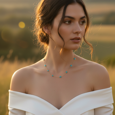 Woman in a white off-shoulder dress with a blurred natural background Elegant turquoise gold necklace on model – fine jewelry for women by Tresor Collection