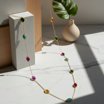 Colorful necklace on a white surface with a vase and leaf in the background Close-up of 18K gold multicolor gemstone necklace – handcrafted fine jewelry from Tresor Collection boutique