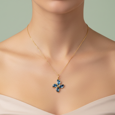 Gold necklace with a blue pendant on a mannequin against a light green background Close-up of London Blue Topaz flower pendant necklace on model’s neck – luxury fine jewelry