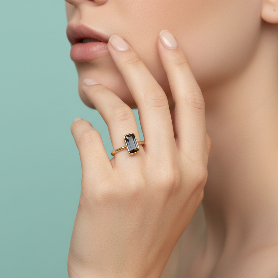 Hand wearing a gold ring with a gemstone on a light green background Model wearing sapphire rectangular-cut ring – sophisticated high-end jewelry look