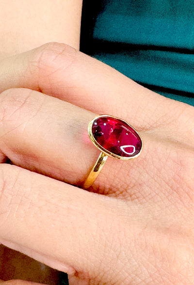 Gold ring with a red gemstone on a person's finger Gold orange sapphire ring worn on hand – vibrant gemstone ring styling inspiration by Tresor Collection