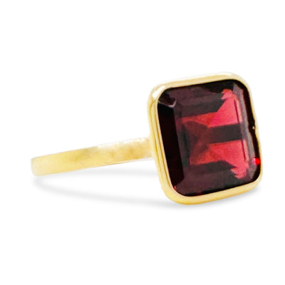 Gold ring with a red gemstone on a white background Side view of 18K gold square-cut rhodolite garnet ring – fine artisan jewelry by Tresor Collection