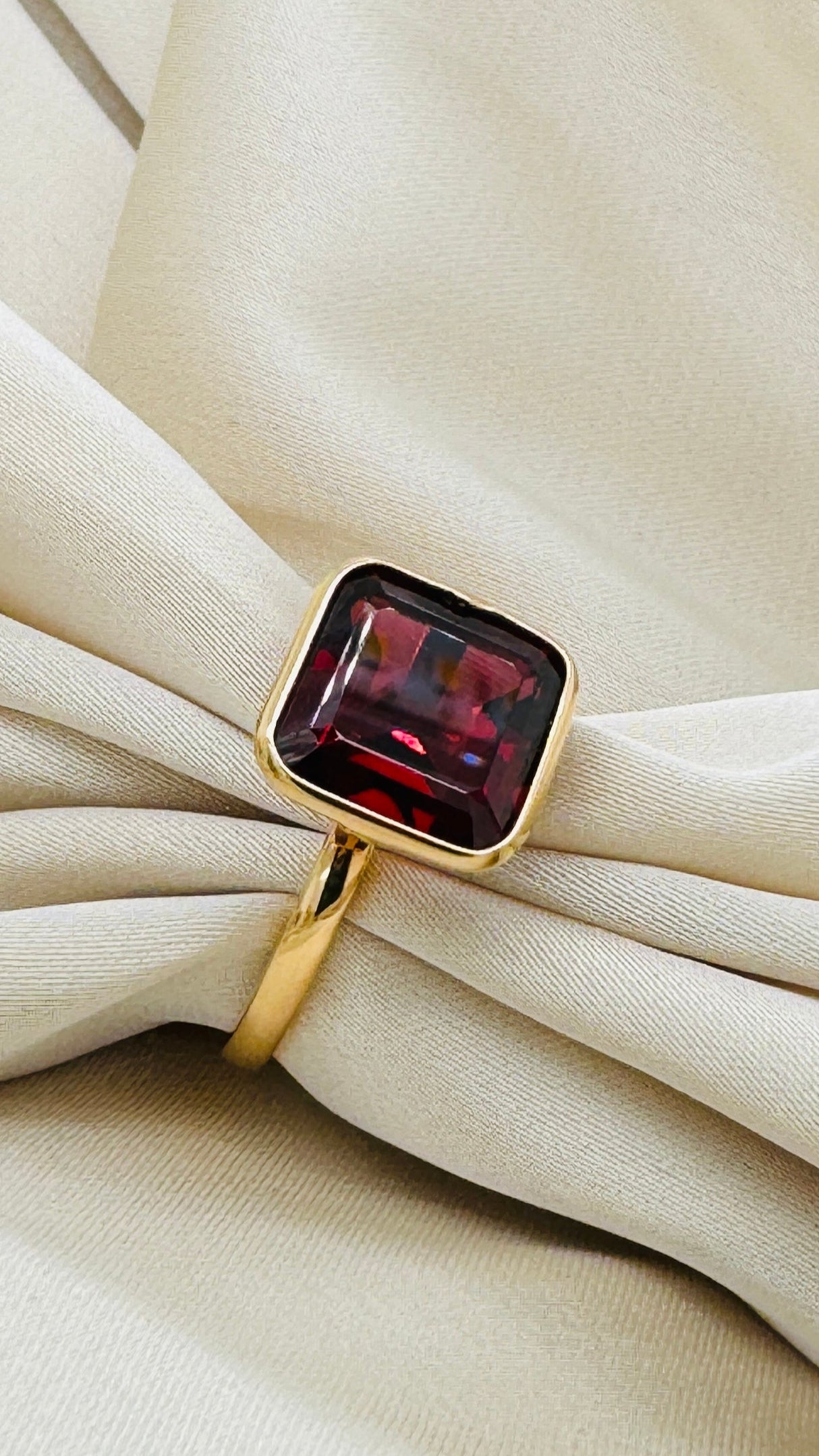 Close-up of square rhodolite garnet ring on beige fabric – luxury gold gemstone ring by Tresor Collection