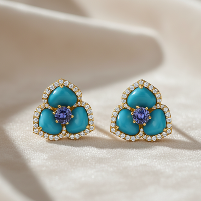 Turquoise flower-shaped earrings with gold and purple gemstones on a beige fabric background Close-up of 18K gold turquoise cabochon floral earrings with sapphire and diamonds