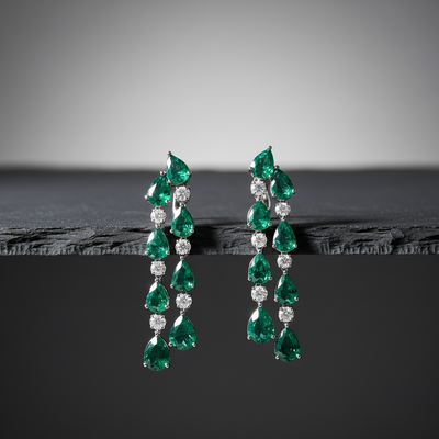 Pair of emerald and diamond earrings on a dark surface with a gray background Artistic flatlay of emerald and diamond drop earrings – handcrafted 18K gold statement jewelry