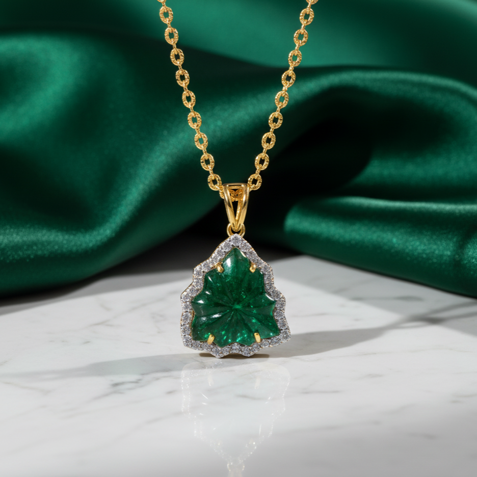 Gold necklace with a green gemstone pendant on a green fabric background Close-up of 18K gold emerald carved pendant – handcrafted fine jewelry from Tresor Collection