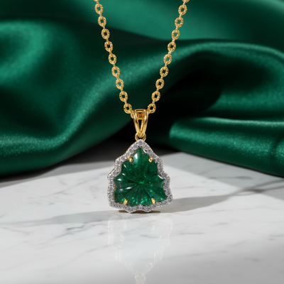 Gold necklace with a green gemstone pendant on a green fabric background Close-up of 18K gold emerald carved pendant – handcrafted fine jewelry from Tresor Collection
