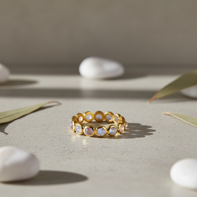 Gold ring with embedded stones on a neutral surface with stones and leaves Close-up of 18K gold rainbow moonstone eternity ring – handcrafted gemstone jewelry from Tresor Collection