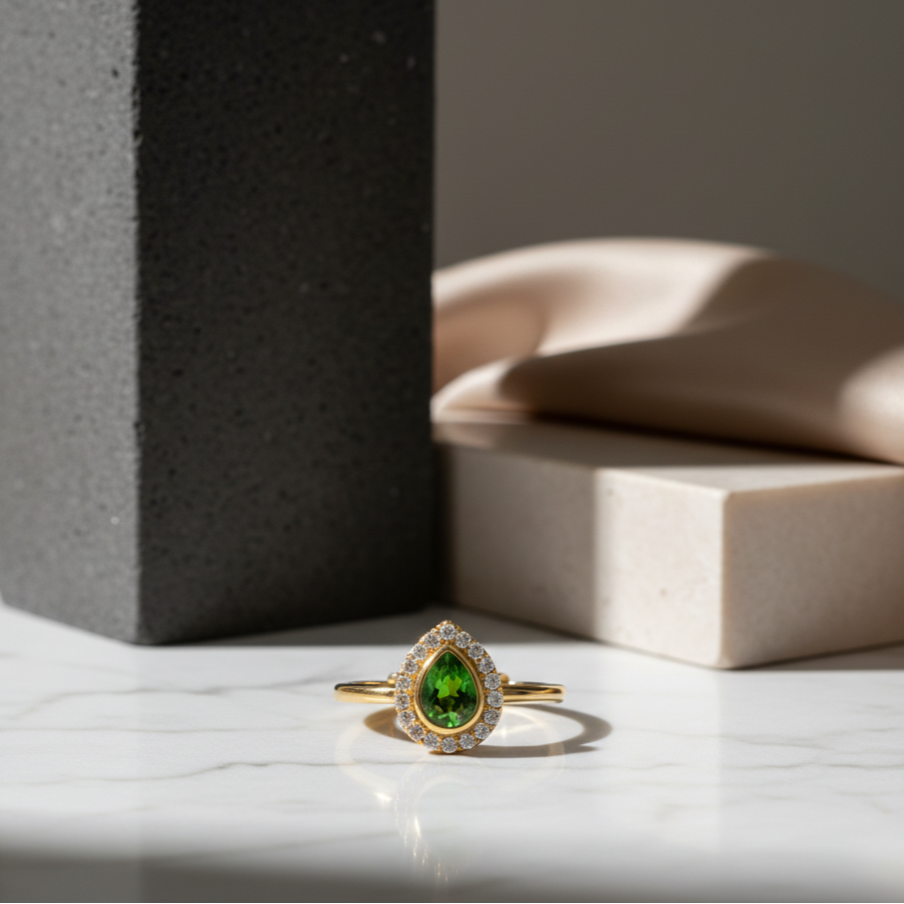Gold ring with a green gemstone on a marble surface Close-up of 18K gold tsavorite and diamond ring – handcrafted fine jewelry from Tresor Collection boutique