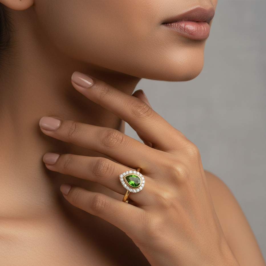 Close-up of a hand wearing a gold ring with a green gemstone on a neutral background Elegant tsavorite and diamond ring on model – designer gold jewelry for women by Tresor Collection