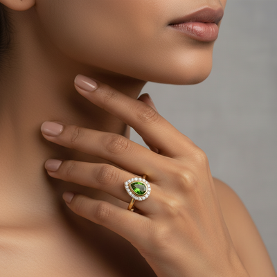 Close-up of a hand wearing a gold ring with a green gemstone on a neutral background Elegant tsavorite and diamond ring on model – designer gold jewelry for women by Tresor Collection