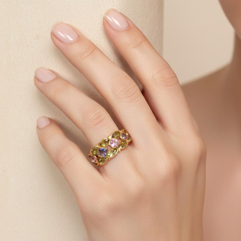 Gold ring with colorful gemstones on a hand against a beige background  Elegant multicolor gemstone ring on model – designer 18K gold jewelry for women by Tresor Collection