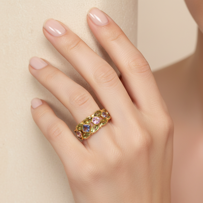 Gold ring with colorful gemstones on a hand against a beige background  Elegant multicolor gemstone ring on model – designer 18K gold jewelry for women by Tresor Collection