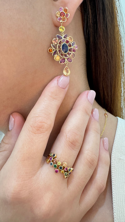 Close-up of a person wearing colorful gemstone earrings and ring. Close-up of 18K gold multi-sapphire statement earrings – luxury handcrafted jewelry by Tresor Collection