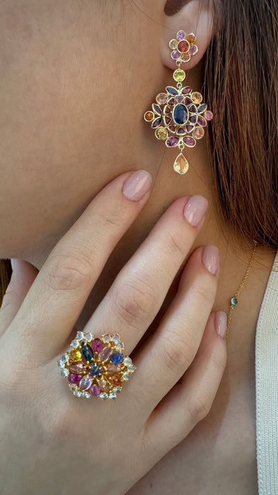 Close-up of a person wearing colorful gemstone earrings and ring. Multi-sapphire drop earrings styled for festive occasions – elegant fine jewelry by Tresor Collection