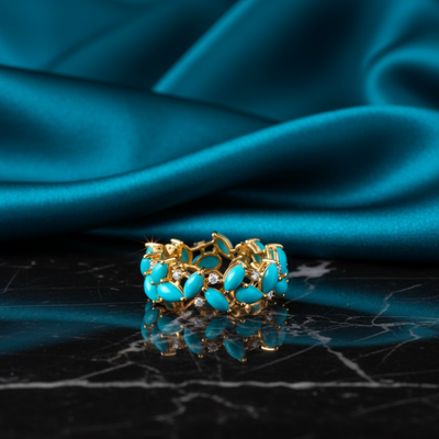 Gold ring with turquoise stones on a black marble surface with teal fabric background Close-up of 18K gold turquoise and diamond ring – handcrafted fine jewelry from Tresor Collection boutique