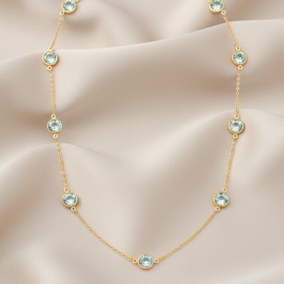 Gold necklace with blue gemstones on a beige fabric background Close-up of 18K gold aquamarine necklace – handcrafted fine jewelry from Tresor Collection boutique