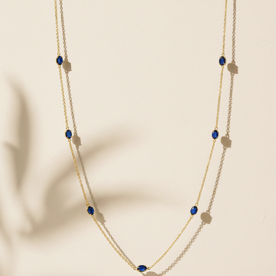 Gold necklace with blue gemstones on a beige background Close-up of 18K gold blue sapphire necklace – handcrafted fine jewelry from Tresor Collection boutique