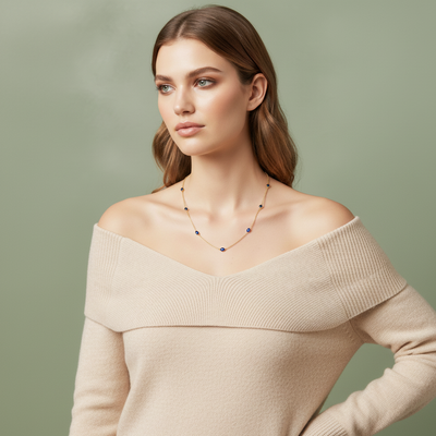 Woman wearing a beige off-shoulder sweater with a necklace on a light green background Blue sapphire necklace styled for everyday elegance – luxury handcrafted jewelry from Tresor Collection