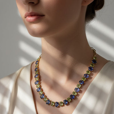 Necklace with multicolored beads worn by a person in a white outfit. Elegant Tanzanite and Tsavorite gold necklace on model – designer statement jewelry for women by Tresor Collection