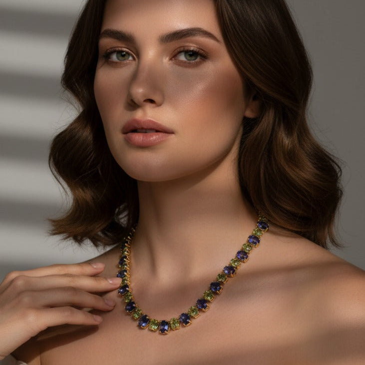 Woman wearing a colorful necklace against a neutral background Statement Tanzanite and Tsavorite necklace styled for festive elegance – luxury fine jewelry from Tresor Collection
