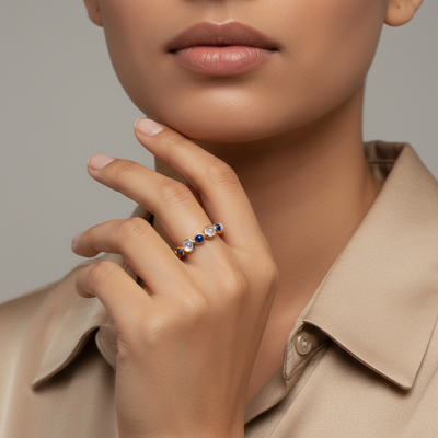 Close-up of a hand wearing a ring with colored gemstones, set against a neutral background. Stackable 18K gold gemstone cabochon rings from Tresor’s Mosaico Collection – modern luxury jewelry
