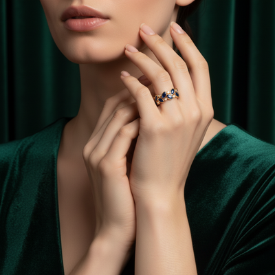 Close-up of a woman's hand wearing a ring with gemstones against a dark green background Blue sapphire gold ring styled for festive occasions – luxury handcrafted jewelry from Tresor Collection